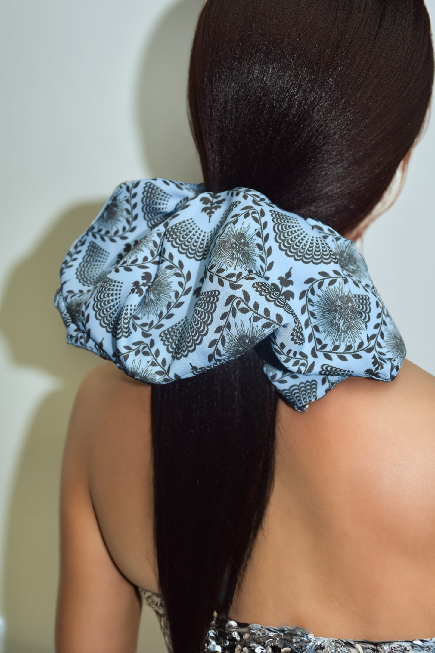 A sky blue scrunchie with a carnival lady print, worn in a ponytail hairstyle by Ayiti Cherie